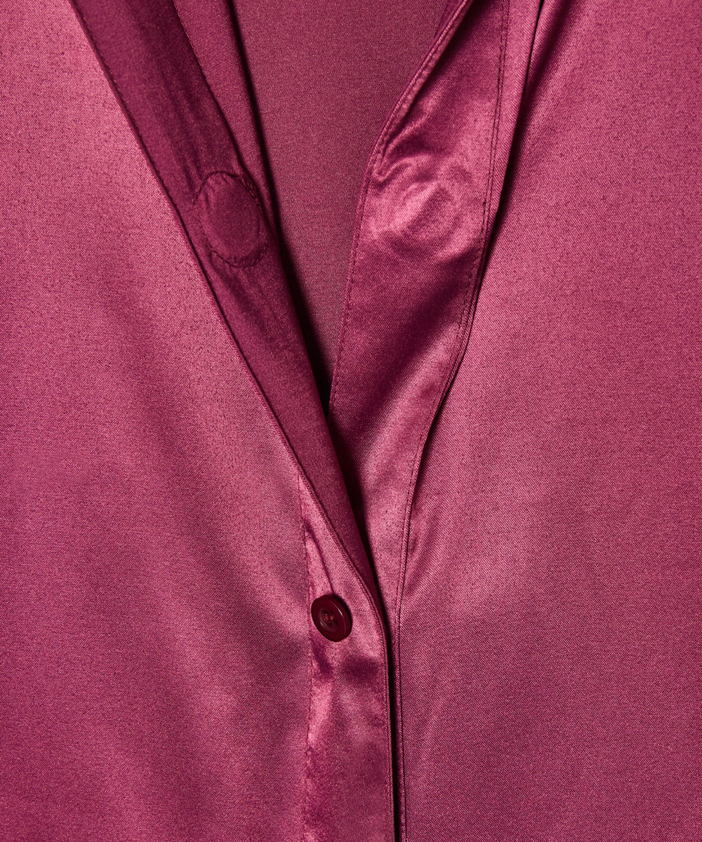 A close-up of a satin or silk button-up shirt in a rich magenta-purple color, showing the smooth texture and a button closure.